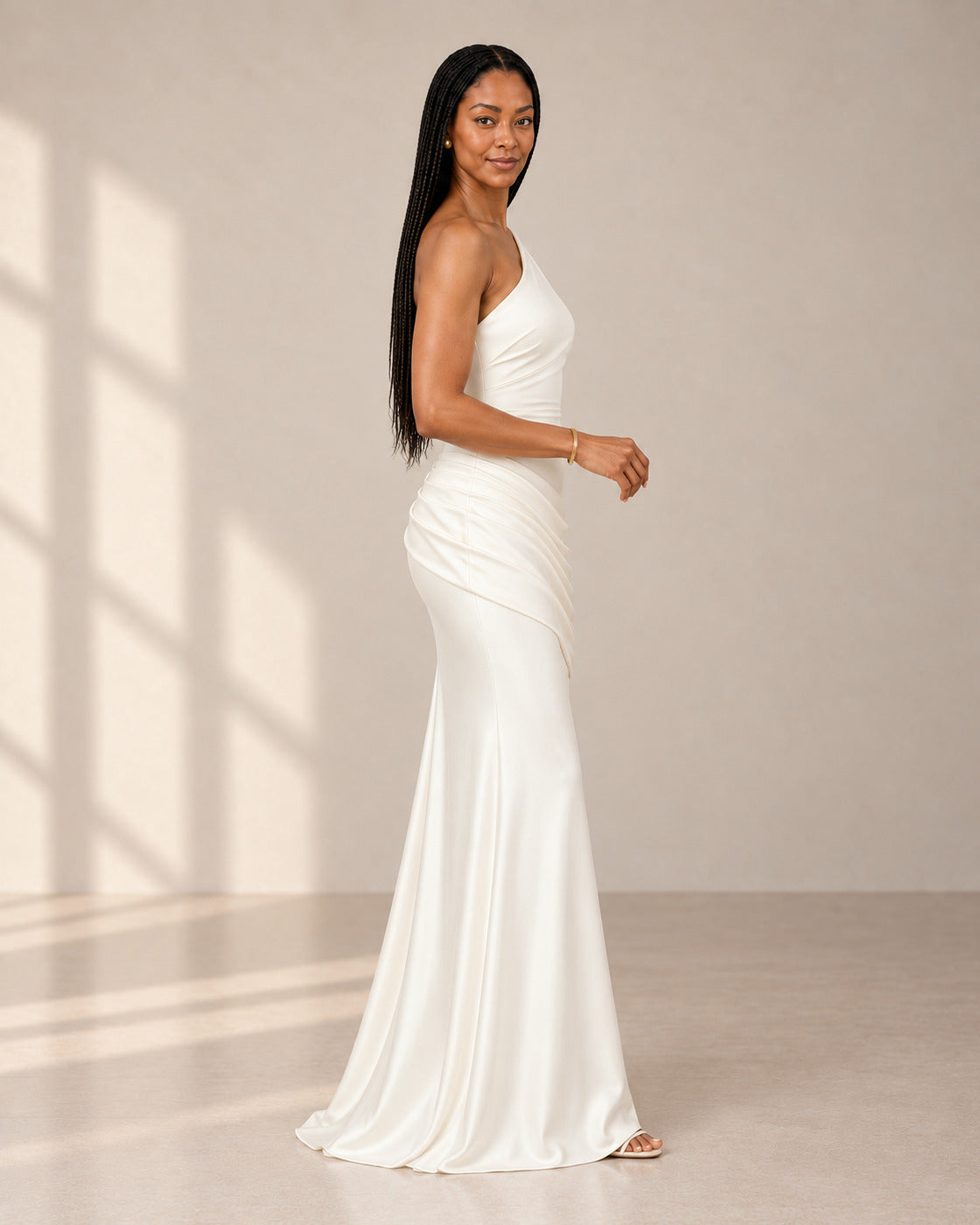 Side view of the Delphine Draped Gown in white, showing its one-shoulder neckline and draped skirt